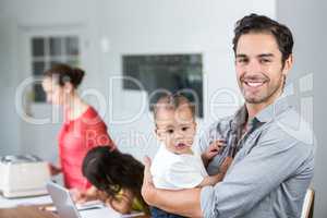 Portrait of smiling father carrying baby at home
