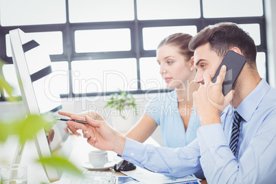 Businessman talking on mobile phone while pointing at computer m