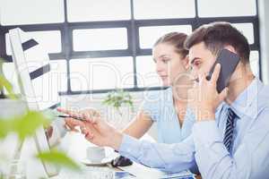 Businessman talking on mobile phone while pointing at computer m