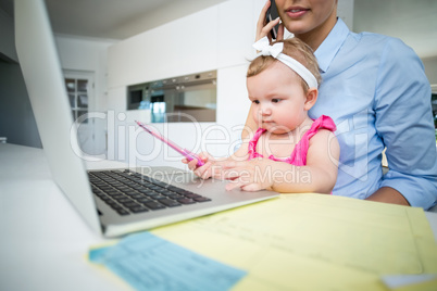 Playful baby girl sitting with mother by laptop