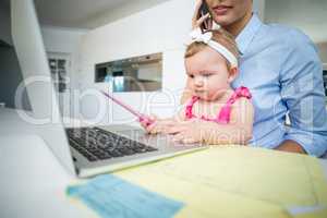Playful baby girl sitting with mother by laptop