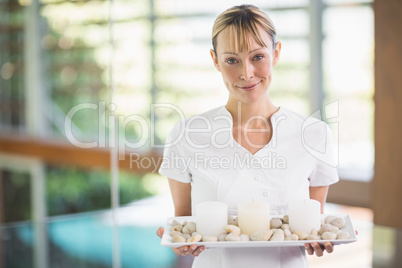 Portrait of smiling masseur holding tray with pebbles and candle