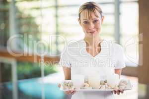 Portrait of smiling masseur holding tray with pebbles and candle