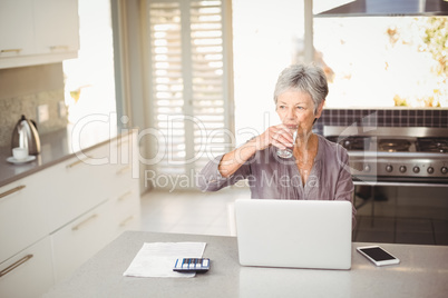 Senior woman drinking water while sitting at table in kitchen