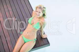 Portrait of beautiful woman in green bikini relaxing by pool sid