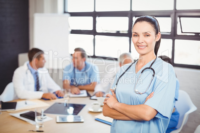 Happy female doctor standing with arms crossed in conference roo
