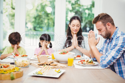 Family praying while sitting at dining table