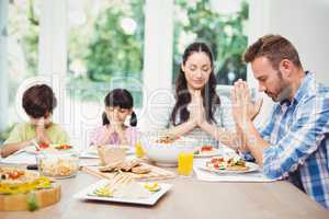 Family praying while sitting at dining table