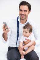 Portrait of smiling father holding mobile phone with baby