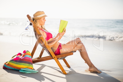 Woman in bikini sitting on armchair and reading book