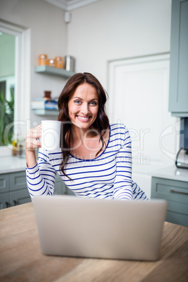 Portrait of smiling woman working on laptop while holding coffee