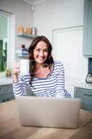 Portrait of smiling woman working on laptop while holding coffee