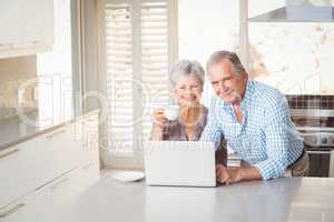 Portrait of senior couple with laptop in kitchen