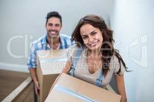 Portrait of smiling couple holding cardboard boxes while climbin