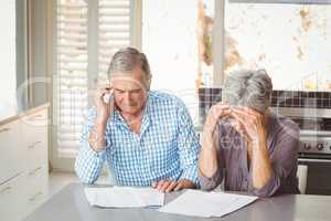 Worried senior couple with documents in kitchen