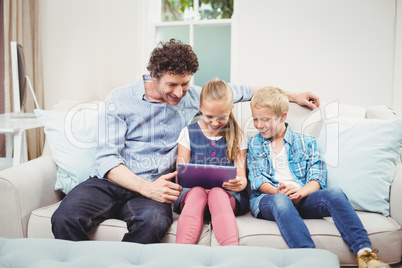 Father with children using digital tablet on sofa