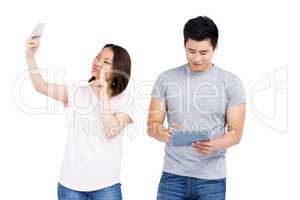 Young woman taking a selfie on smartphone and man using digital