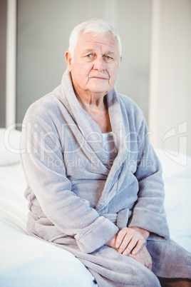 Portrait of suffering senior man sitting on bed