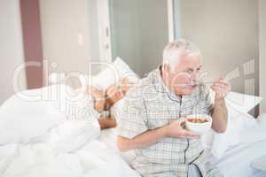 Senior man eating salad by sleeping wife