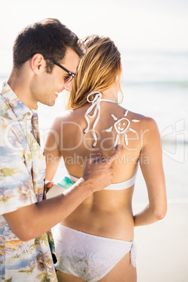 Man making a sun symbol on womans back while applying a sunscree