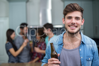 Smiling man holding beer bottle while friends in background