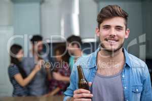 Smiling man holding beer bottle while friends in background