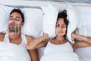 Woman blocking ears while man snoring on bed