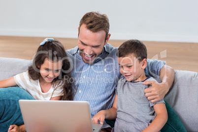 Father sitting with son and daughter and using laptop