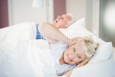 Senior woman blocking ears while man snoring on bed