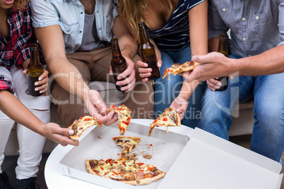 Friends holding beer while eating pizza at home