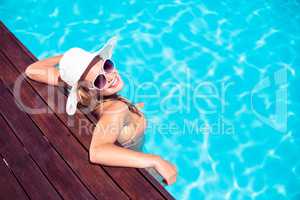 Beautiful woman wearing sunglasses and straw hat leaning on wood