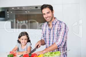 Portrait of smiling father cutting vegetables with daughter