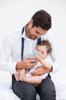 Smiling father holding mobile phone with baby