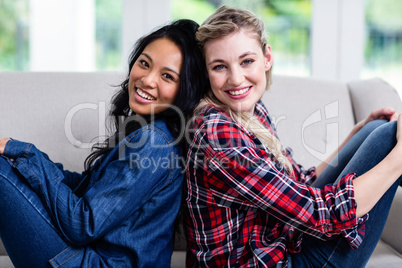 Happy beautiful female friends sitting back to back