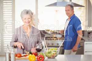 Happy senior woman cutting vegetables with husband in background