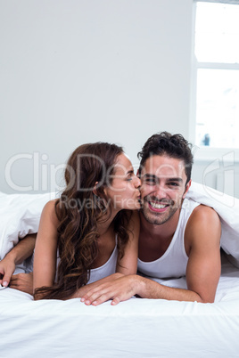 Woman kissing man while lying under blanket