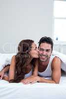 Woman kissing man while lying under blanket