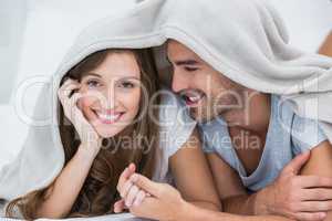 Smiling couple lying under blanket