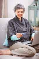 Mature woman looking at credit card while using laptop