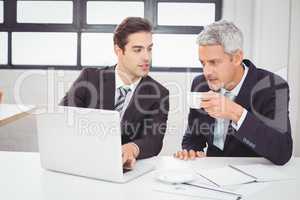 Businessman having coffee while working with colleague