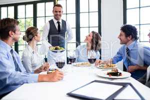 Waiter serving salad to business people