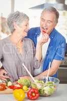 Happy senior woman feeding husband while standing at counter