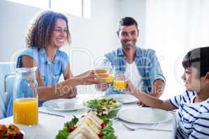 Family toasting glasses of orange juice while having breakfast