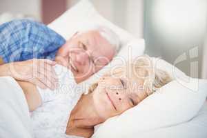 Portrait of smiling senior woman relaxing besides man on bed