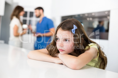 Sad girl leaning on table against arguing parents