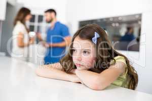 Sad girl leaning on table against arguing parents
