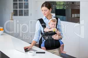 Woman carrying baby girl while using laptop at table
