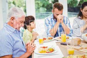 Multi generation family praying while sitting at dining table