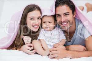 Portrait of smiling couple with baby on bed