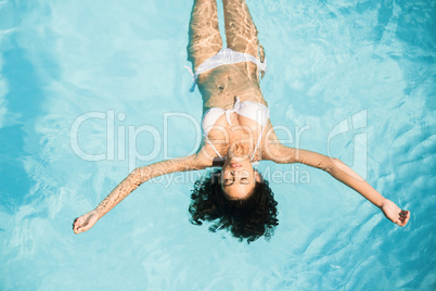 Beautiful woman in white bikini floating in swimming pool